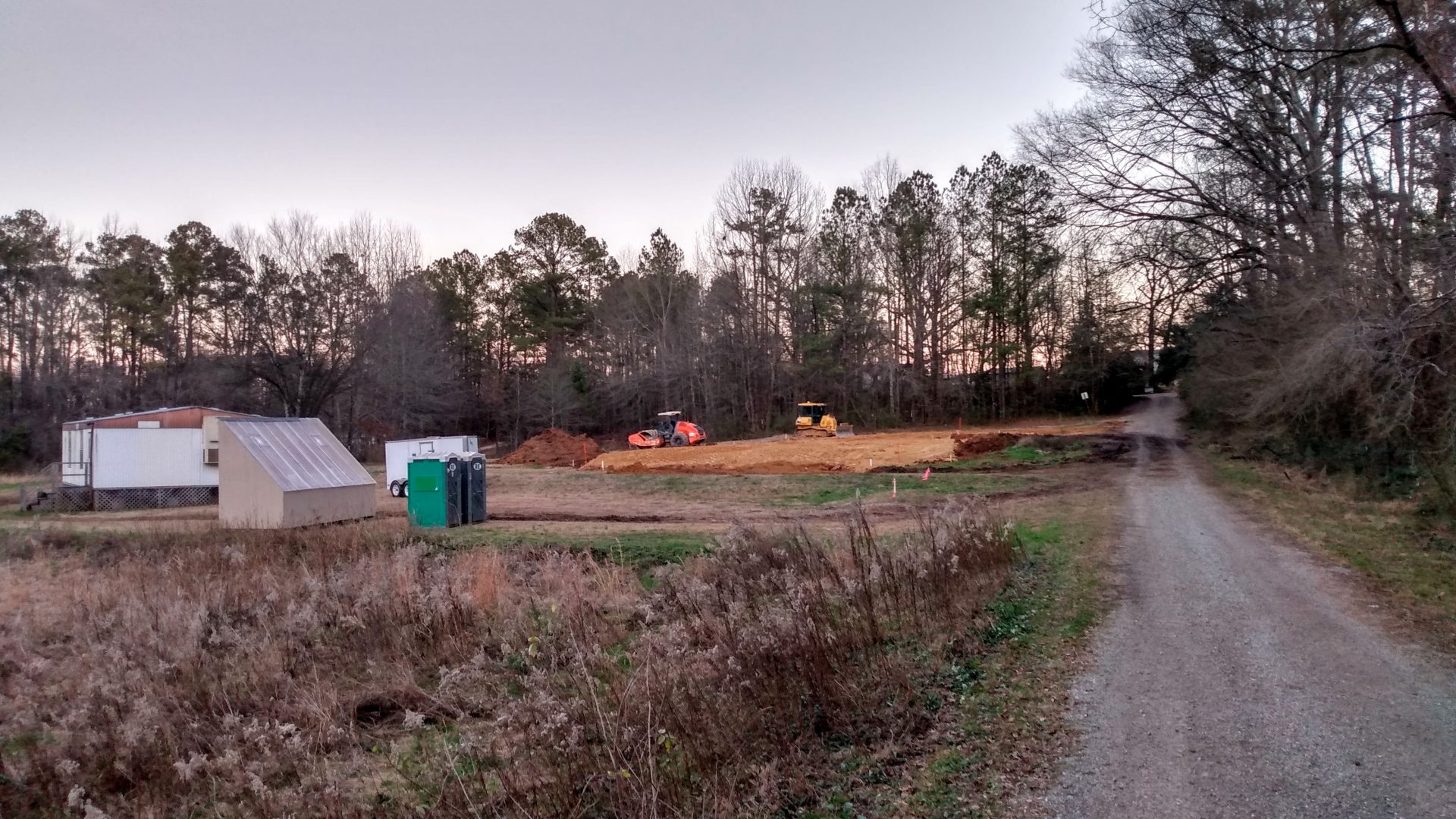 Field in foreground with classroom trailer, solar kiln, and construction site in background.